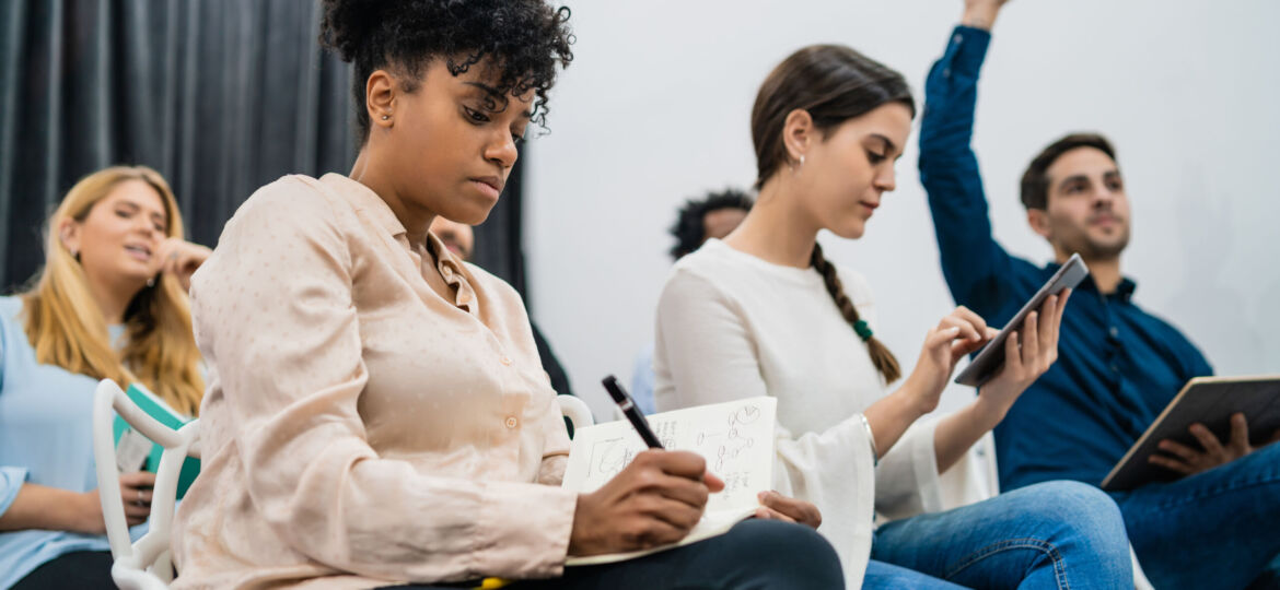 Group of young people sitting on conference together while raising their hands to ask a question. Business team meeting seminar training concept.